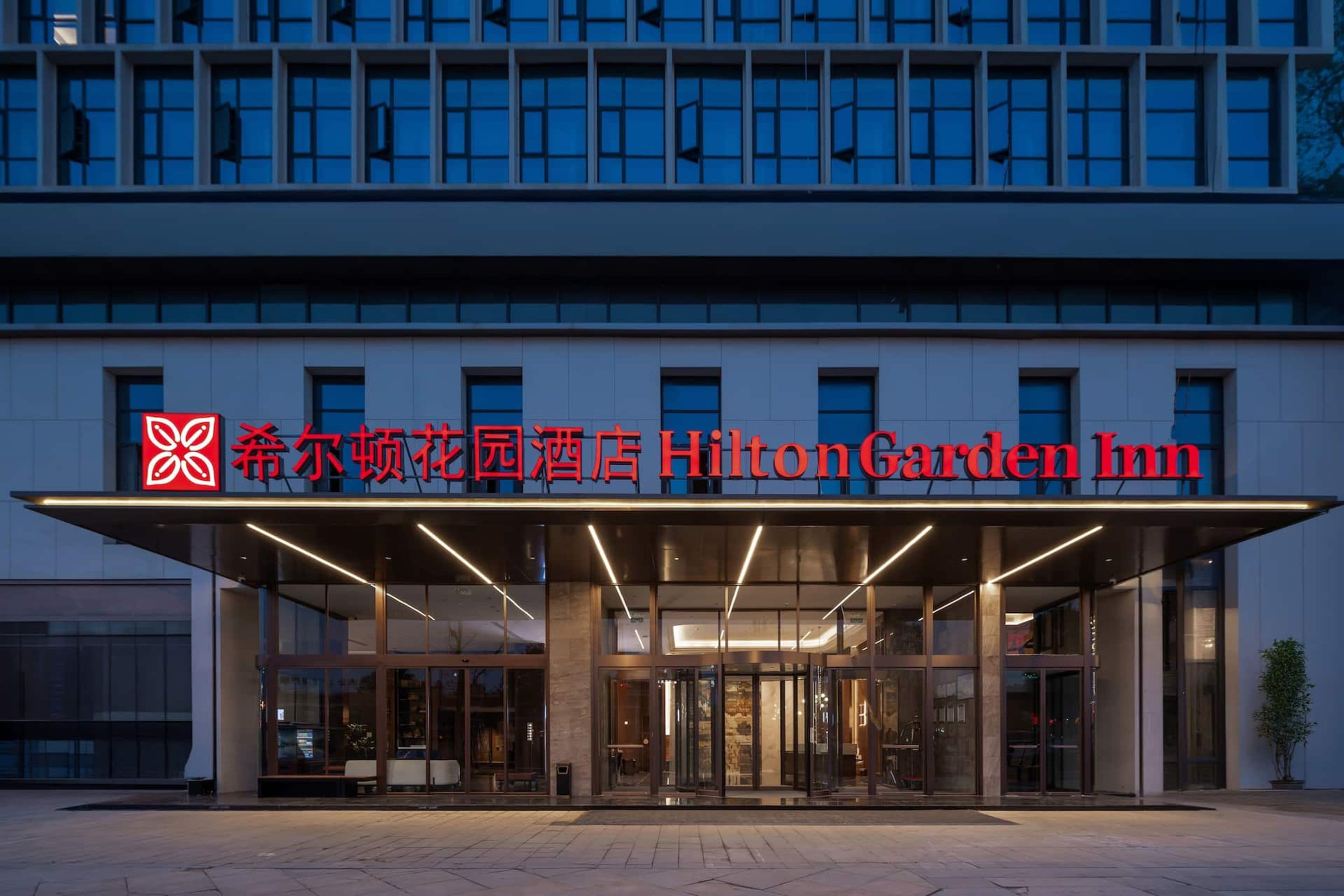 El exterior del Hilton Garden Inn presenta una fachada moderna, un amplio acceso de vidrio y señalización destacada.