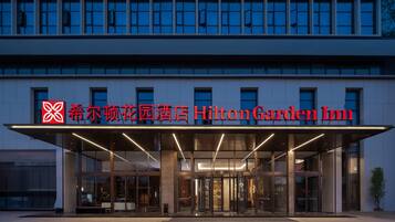 El exterior del Hilton Garden Inn presenta una fachada moderna, un amplio acceso de vidrio y señalización destacada.