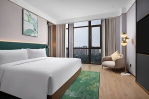 A modern hotel room with a large bed, a view of the city through floor-to-ceiling windows, a green area rug, and a side table with a lamp. - Hilton Garden Inn Leshan Shizhong (Leshan)