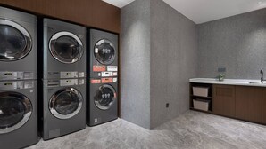 A laundry room with four stacked front-loading washing machines, a sink, and a small plant on the countertop. - Hilton Garden Inn Leshan Shizhong (Leshan)