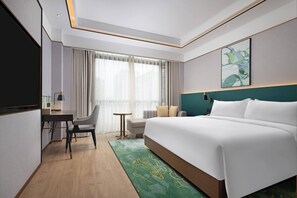 A hotel room with a large bed, a desk, a chair, a small table, and a window with curtains. - Hilton Garden Inn Leshan Shizhong (Leshan)