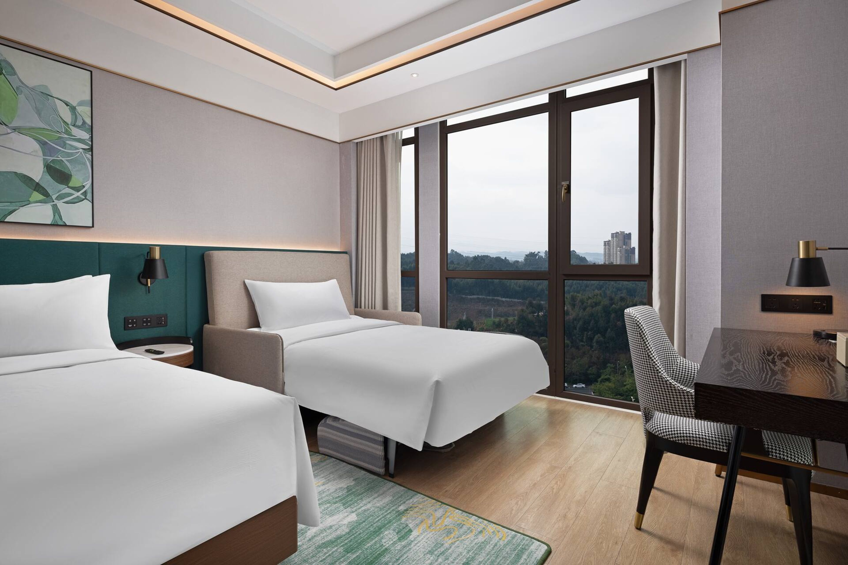 A hotel room with two beds, a desk, and a chair. There is a large window with a view of buildings and trees.