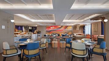 Een modern restaurant met een centraal eetgedeelte met ronde tafels en blauwe stoelen, een bar met krukken, en een grote abstracte muurschildering op de achterwand.