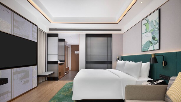 A modern hotel room with a large bed, a sofa, a desk, and a TV. - Hilton Garden Inn Leshan Shizhong (Leshan)