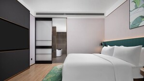 A modern hotel room with a large bed, a green patterned rug, a dark wardrobe, and a white headboard. - Hilton Garden Inn Leshan Shizhong (Leshan)