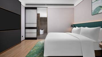 Een moderne hotelkamer met een groot bed, een vloerkleed met groen patroon, een donkere garderobe en een wit hoofdeinde.
