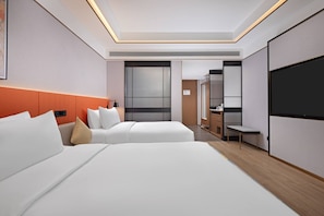 Habitación de hotel con dos camas, televisión, escritorio y baño visible al fondo.