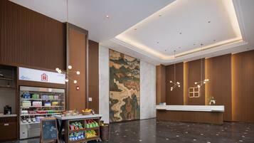 A modern hotel lobby with a reception desk, a beverage kiosk, and a large camouflage-patterned wall.