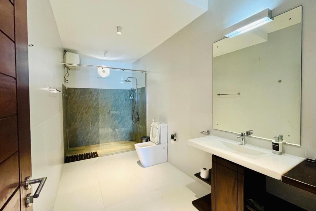 A modern bathroom with a glass-enclosed shower, a white sink, and a large mirror.