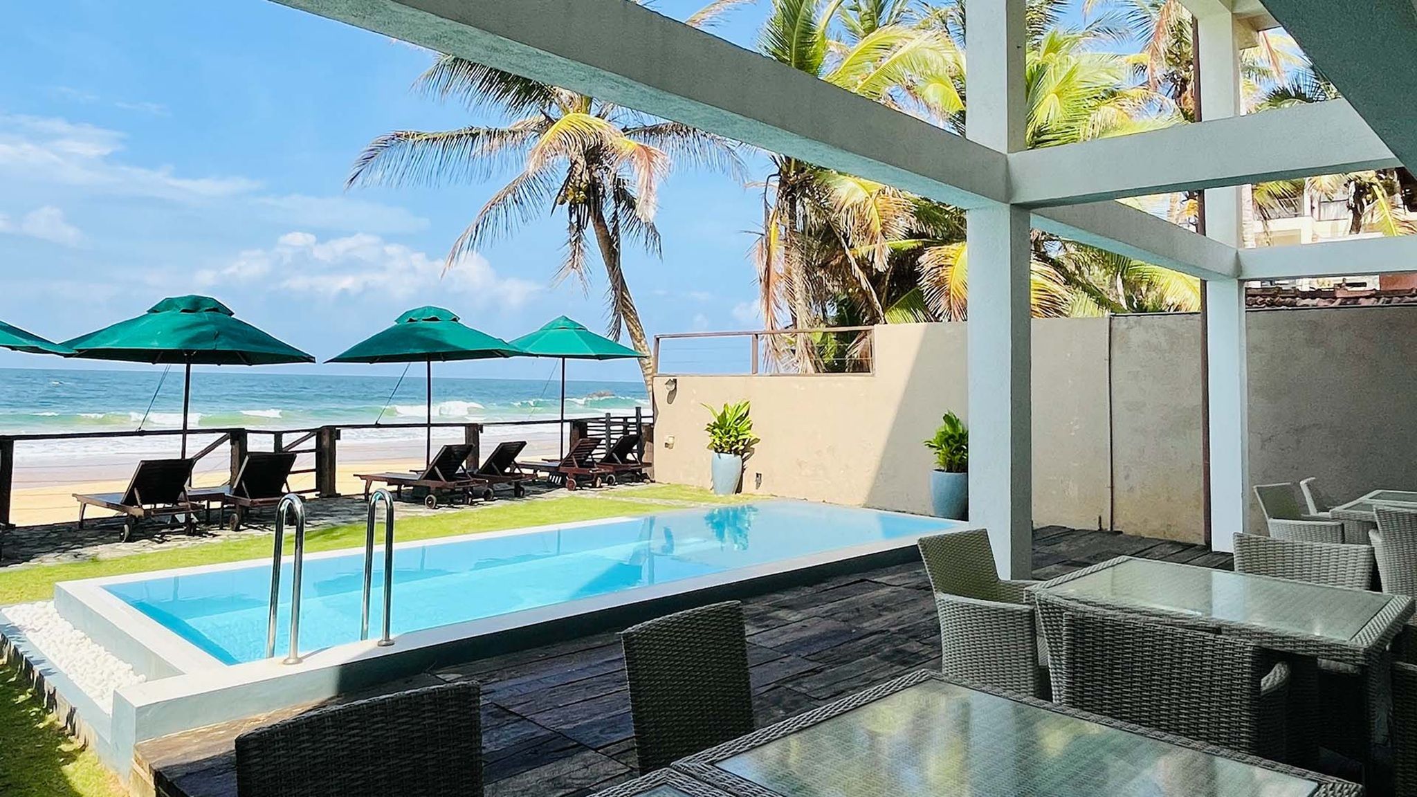 A pool area with lounge chairs and umbrellas, overlooking the beach and ocean.