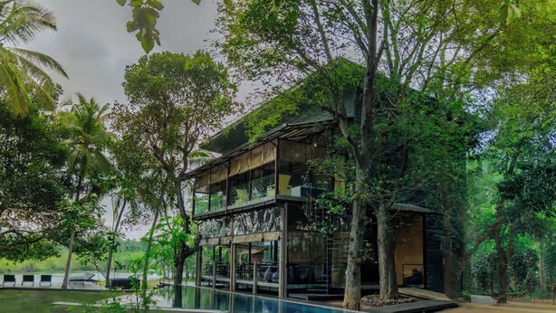 A modern building with a glass facade, surrounded by lush greenery and a swimming pool. - Waraka - Udawalawe By Thema Collection (Udawalawa)