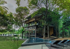 Un bâtiment moderne à la façade vitrée, entouré d’une végétation luxuriante et agrémenté d’une piscine.