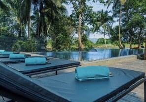 Un espace aménagé au bord de la piscine, avec des chaises longues et une vue sur un élément aquatique entouré d’une végétation luxuriante.