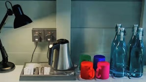 A kitchen counter with a coffee maker, a kettle, a kettle tray, a black desk lamp, and colorful mugs. - Waraka - Udawalawe By Thema Collection (Udawalawa)