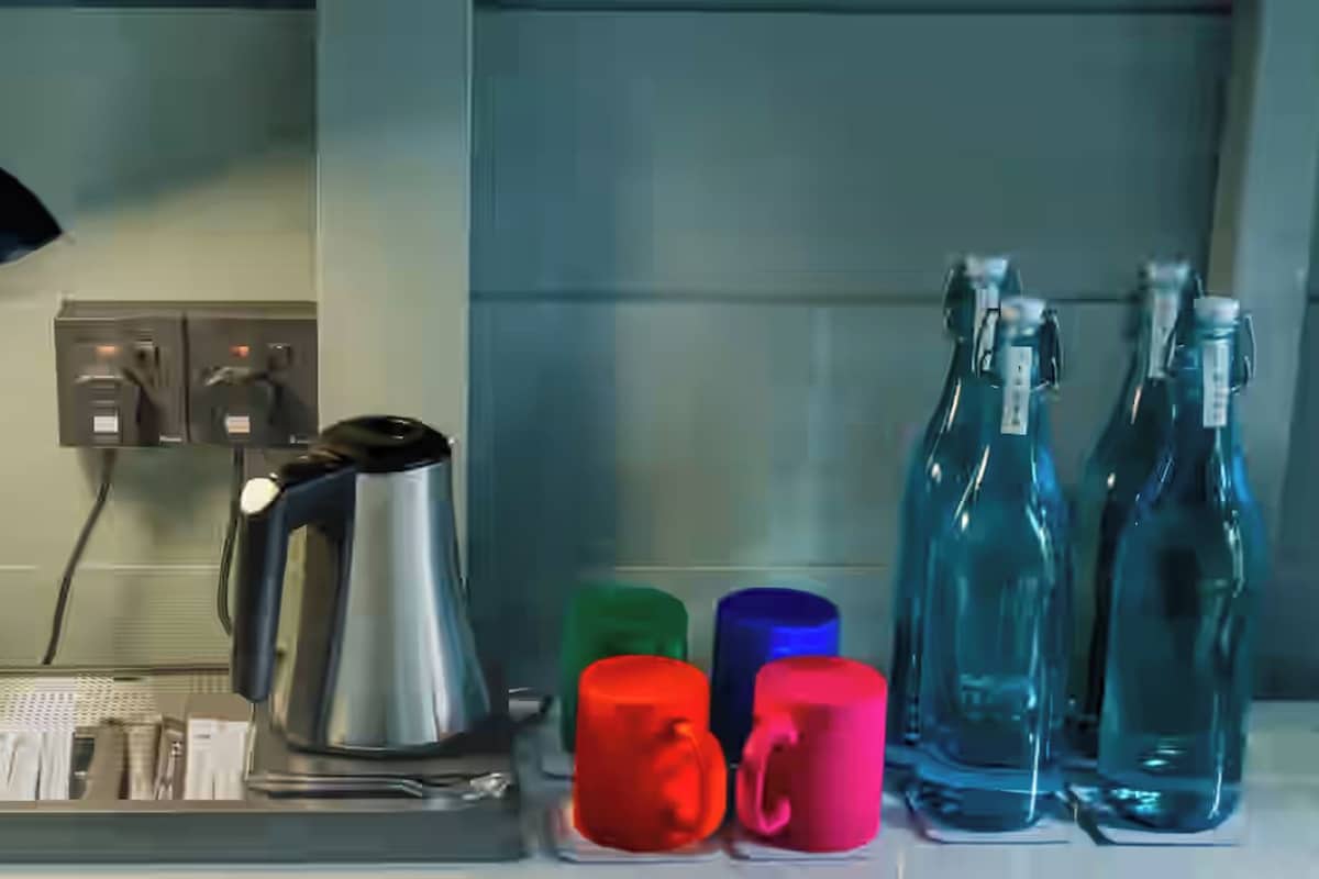 A kitchen counter with a coffee maker, a kettle, a kettle tray, a black desk lamp, and colorful mugs.
