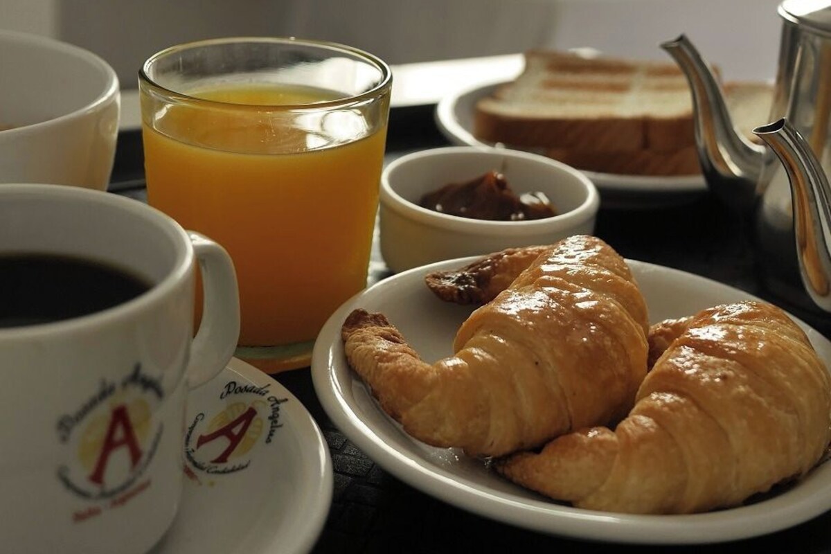 Een ontbijttafel met croissants, sinaasappelsap, koffie en een theepot.