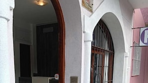 Ein Gebäudeeingang mit Fliesenboden, Holztür und Metallgitter.