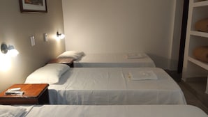 A hotel room with two single beds, a nightstand, a wall-mounted lamp, and a shelf with folded towels. - Paseo Guemes Hotel (Salta)