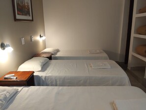 Une chambre d ’hôtel avec deux lits simples, une table de chevet, une lampe fixée au mur et une étagère avec des serviettes pliées.