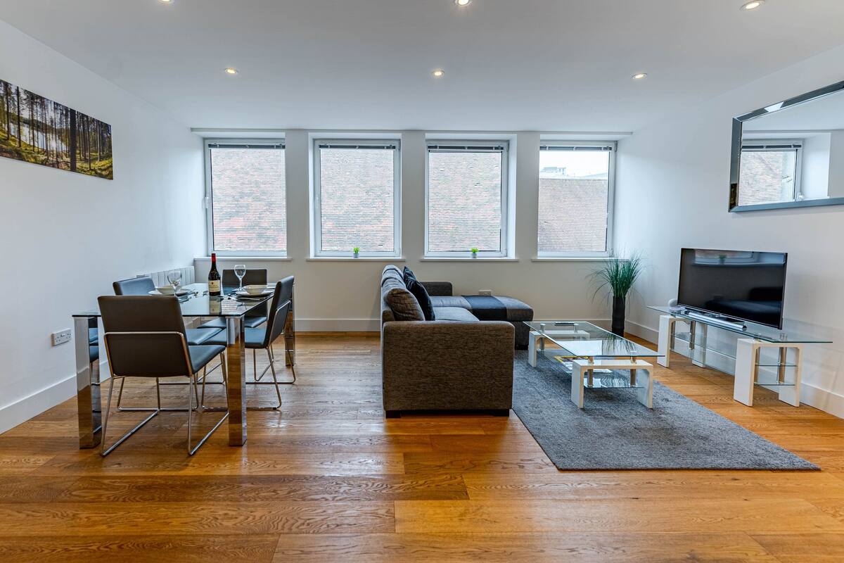Un salón moderno con comedor, ventanas amplias, televisor de pantalla plana y un espejo grande.