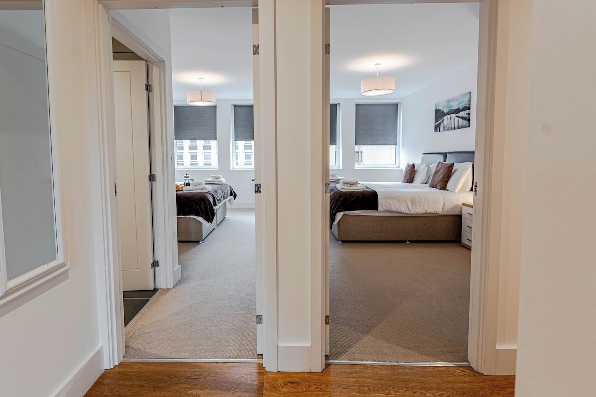 Habitación de hotel con dos camas, un ventanal grande y vistas a la ciudad.