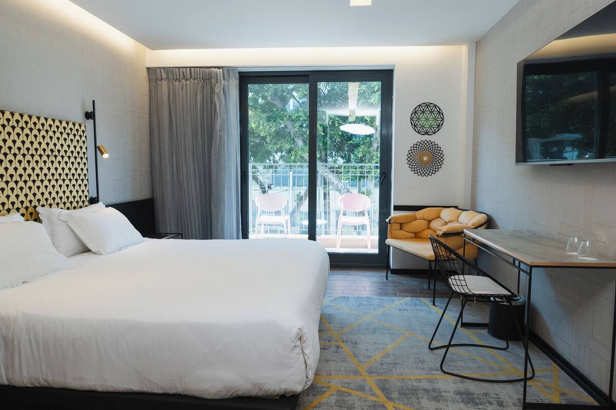 Ein Hotelzimmer mit einem großen Bett, einem Schreibtisch, einem Sessel, einem Fernseher und einem Balkon mit Sitzgelegenheit.
