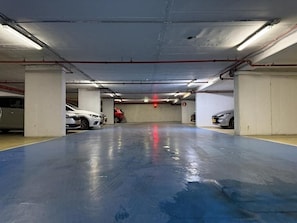 Un estacionamiento de varios niveles con pilares de concreto, suelo azul e iluminación colgante.