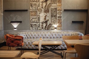 Een moderne zithoek met een gestofte bank, houten tafels en een unieke wand met klassieke reliëfbeeldhouwwerken.
