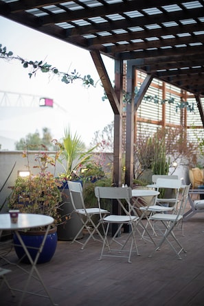 Un patio al aire libre con mesas y sillas, rodeado de plantas en macetas y una pérgola de madera.