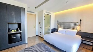 Een moderne hotelkamer met een bed, een minibar, een bureau en een inloopkast.