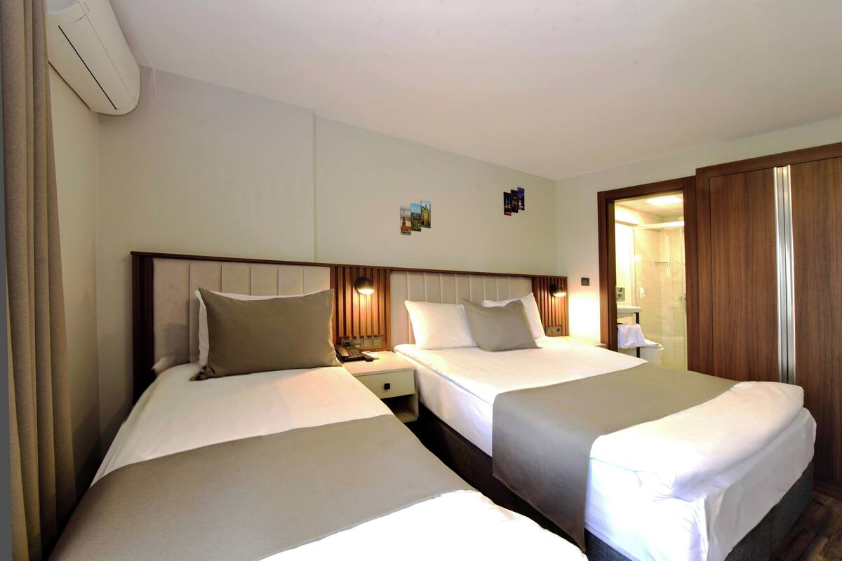 Ein Hotelzimmer mit zwei Betten, einem Nachttisch, einer wandmontierten Klimaanlage und einer Badezimmertür.