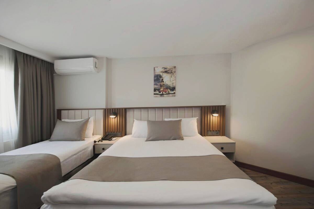 Ein Hotelzimmer mit zwei Einzelbetten, einem großen Bett, einer Klimaanlage, einem Bild an der Wand und einem Nachttisch mit Lampe.