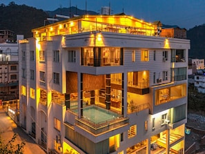 A multi-story hotel with balconies, a swimming pool, and a view of the surrounding area. - Moustache Rishikesh Luxuria (Narendranagar)