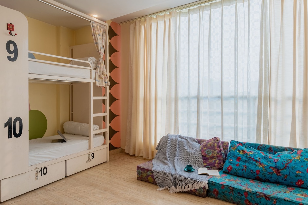 A room with bunk beds labeled 9 and 10, a sofa, and a window with curtains.
