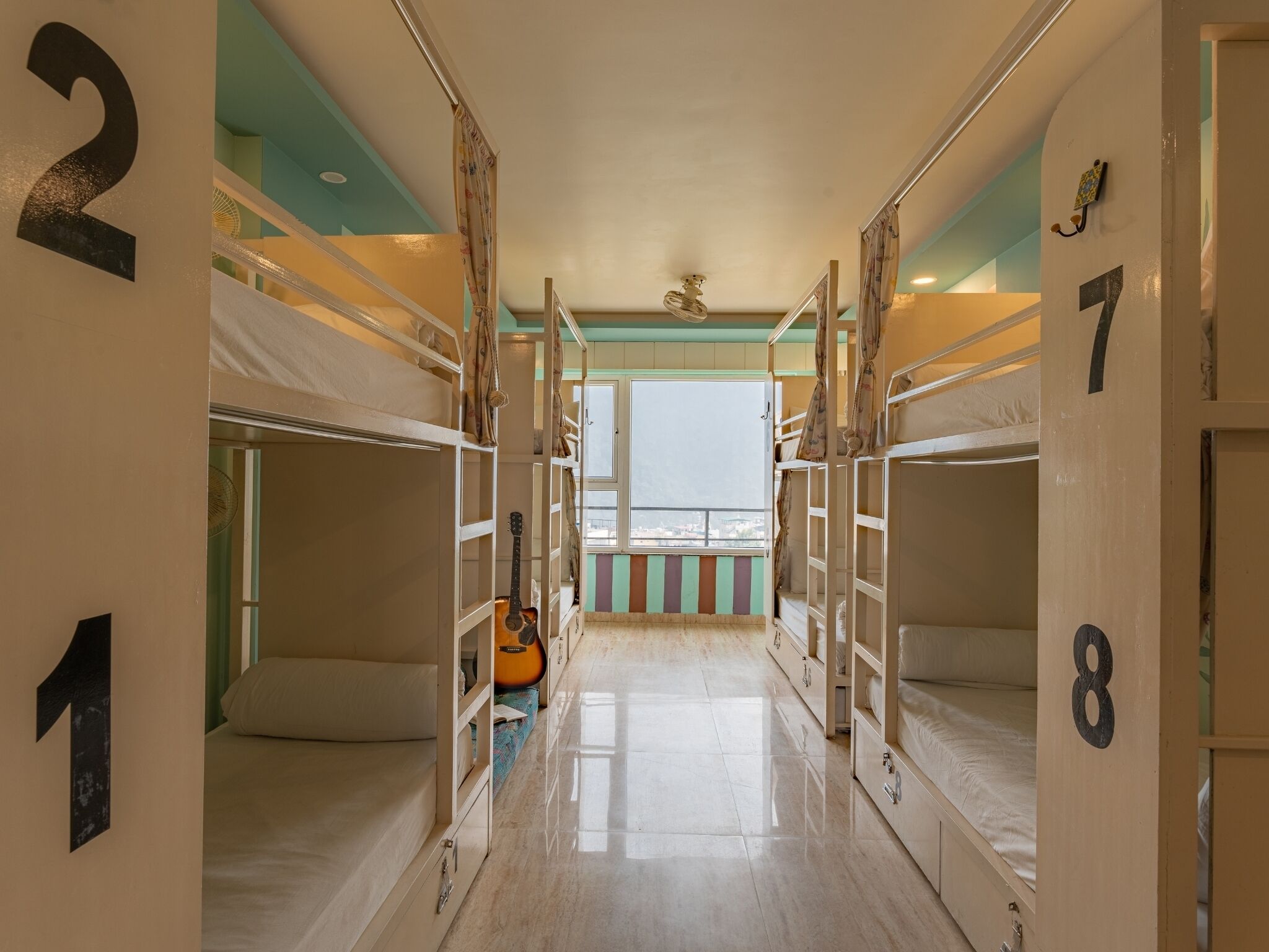A corridor with bunk beds numbered 1 to 8, a guitar, and a view to the outside.