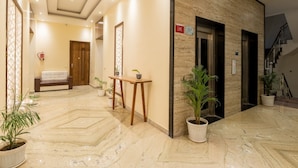 A hotel lobby with a marble floor, a sofa, a wooden table, and potted plants. - Moustache Rishikesh Luxuria (Narendranagar)