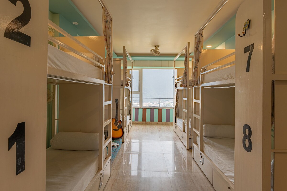 A corridor with bunk beds numbered 1 to 8, a guitar, and a view to the outside.