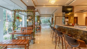 A restaurant with wooden tables and chairs, a check-in desk, and a view of greenery outside. - Moustache Rishikesh Luxuria (Narendranagar)