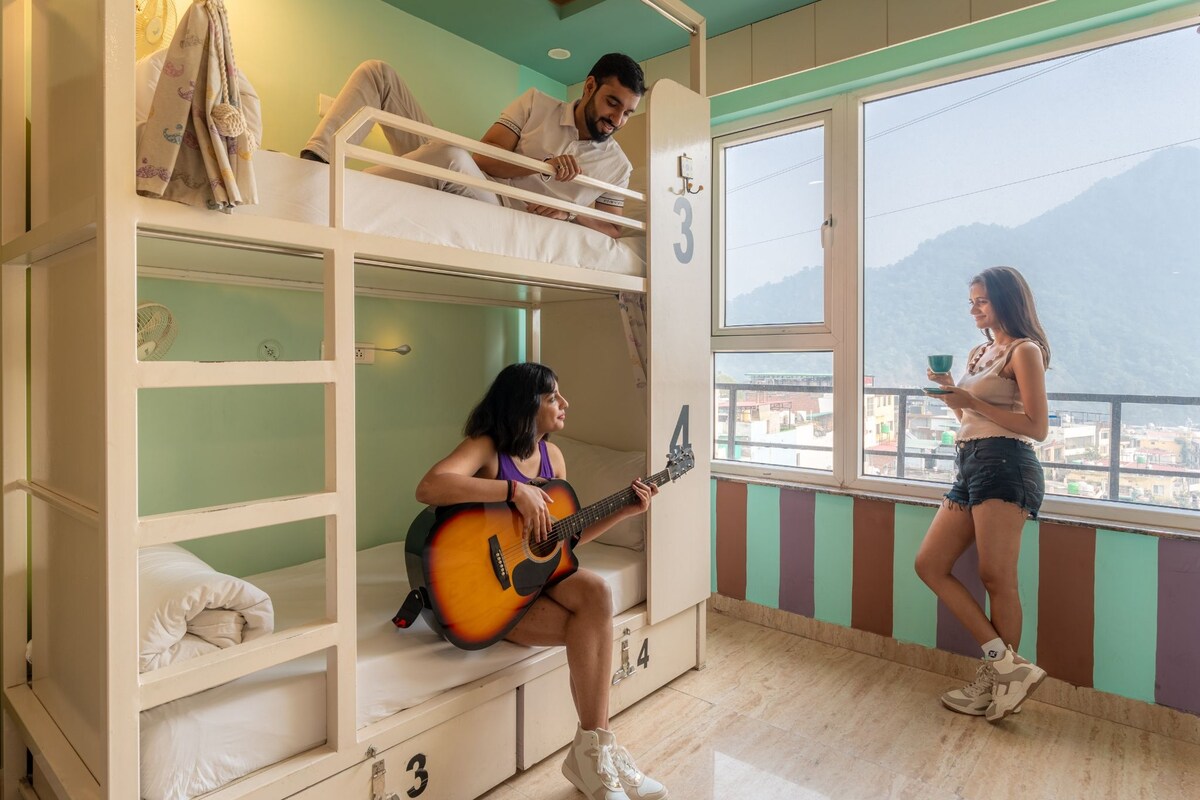 A dormitory room with bunk beds, a window with a view, and a person playing a guitar.