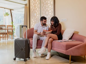A couple sitting on a pink sofa, reading a magazine. A suitcase is on the floor beside them. - Moustache Rishikesh Luxuria (Narendranagar)