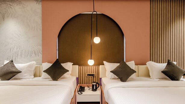 A modern hotel room with two beds, a nightstand, a coffee maker, and a wall-mounted lamp. - Legacy Inn, Mysore (Mysore)