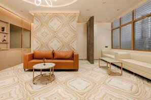 A modern hotel lobby with a patterned floor, a brown leather sofa, a small round table, and a white sofa. - Legacy Inn, Mysore (Mysore)