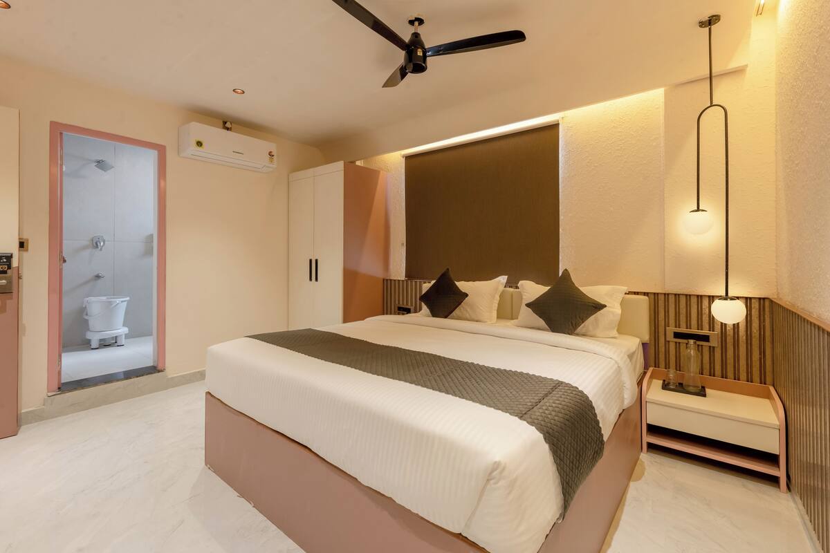 Un dormitorio moderno con una cama grande, un ventilador de techo, una mesita de noche con lámpara y un equipo de aire acondicionado en la pared.