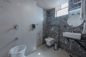 A bathroom with a white toilet, a sink, a mirror, a shower, and a bucket. - Legacy Inn, Mysore (Mysore)