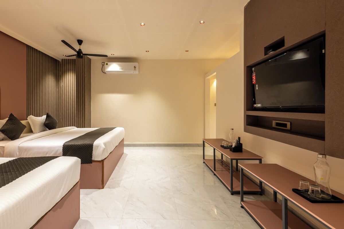 A hotel room with two beds, a ceiling fan, a flat-screen TV, a minibar, and a large mirror.