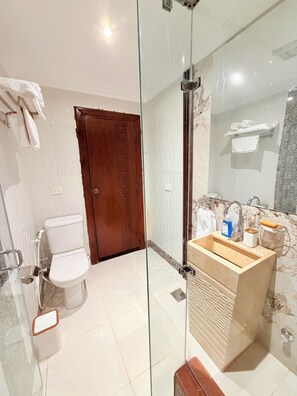 A bathroom with a glass partition, a wooden door, a toilet, a sink with a marble countertop, and a towel rack. - Eco Green Hotel (Giza)