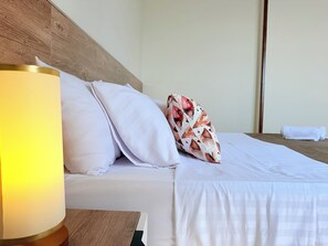Een net opgemaakt bed met witte lakens, een kussen met een patroon en een bedlampje.