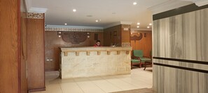 A reception area with a stone counter, wooden paneling, and a green chair. - Eco Green Hotel (Giza)