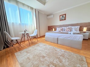 A modern hotel room with a large bed, a small table, two chairs, a large window with curtains, and a wooden floor. - Eco Green Hotel (Giza)