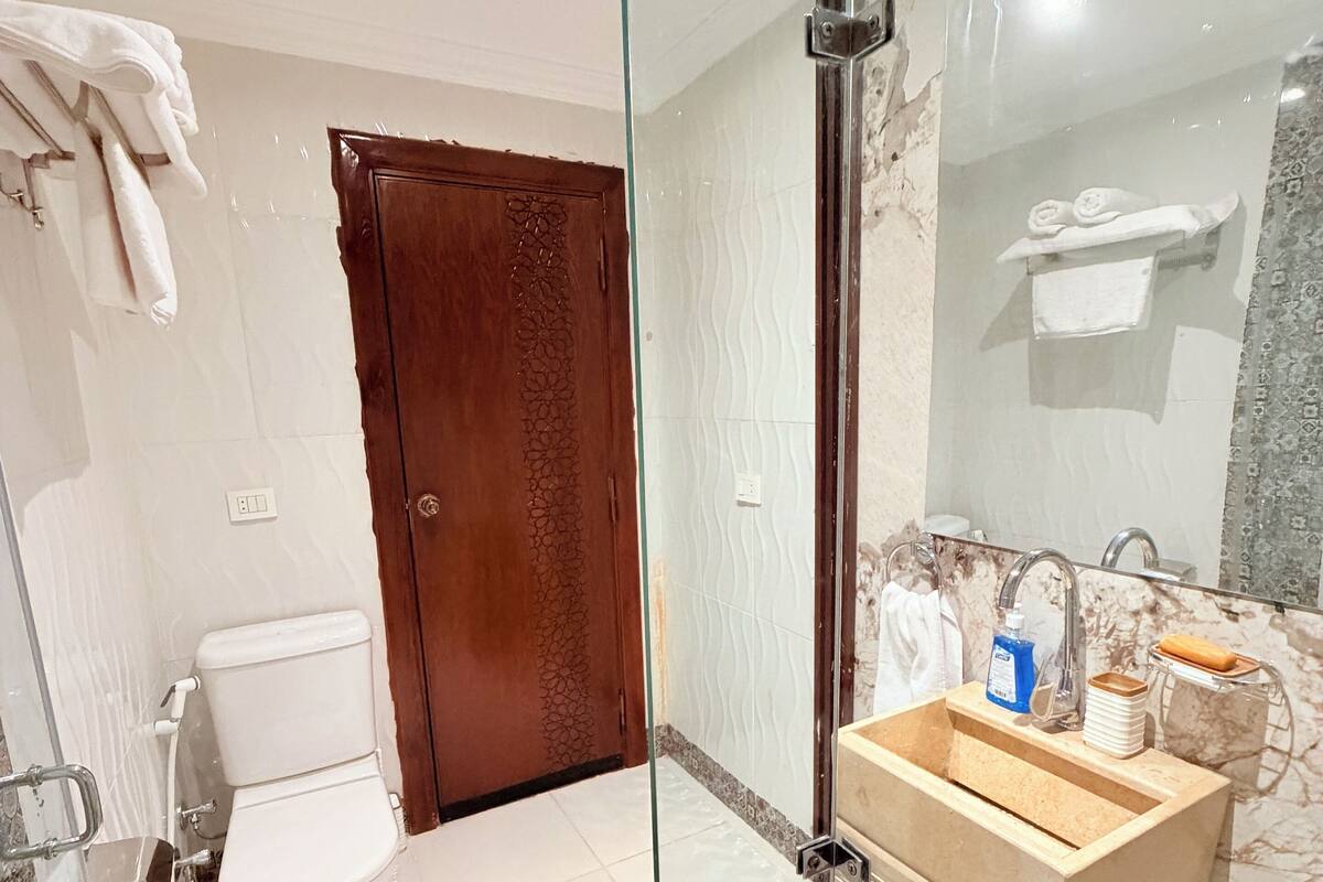 Un baño con mampara de vidrio, puerta de madera, inodoro, lavabo con encimera de mármol y barra para toallas.